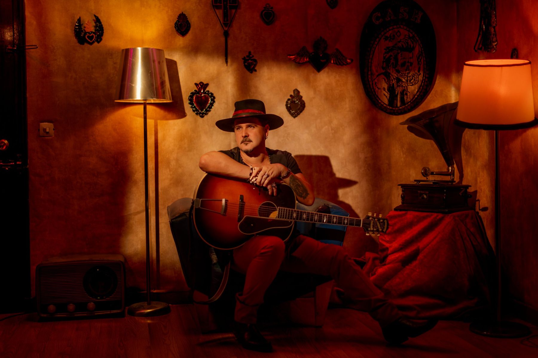 Erik López con sombrero negro apoyado en una guitarra acústica junto a un gramófono